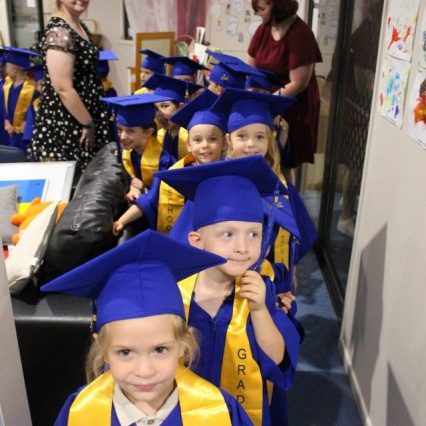 Kids lining up to get their certificates in their graduation uniform - Your ELC
