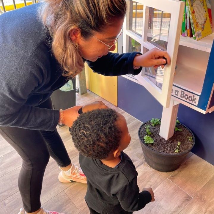A teacher introducing the new book library to a child - Doolandella Early Learning Centre