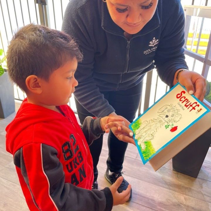 Teacher showing a book to a child - Doolandella Early Learning Centre